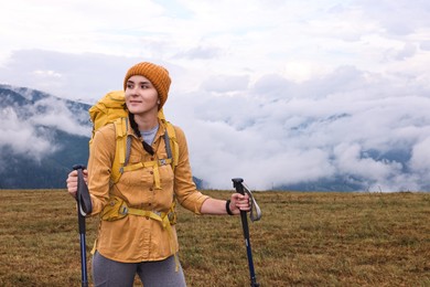 Young hiker with trekking poles and backpack in mountains outdoors, space for text