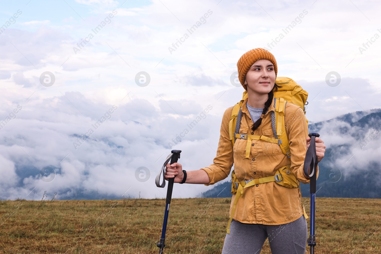 Photo of Young hiker with trekking poles and backpack in mountains outdoors, space for text