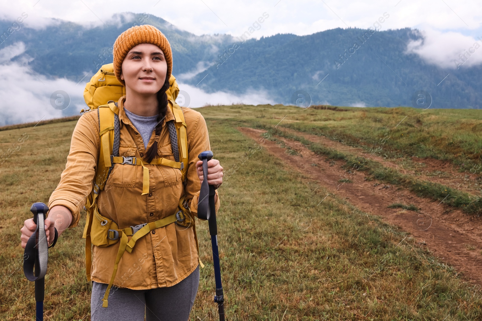 Photo of Young hiker with trekking poles and backpack in mountains outdoors, space for text