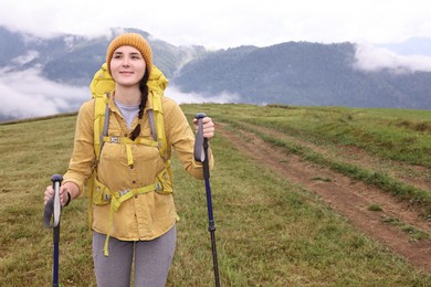 Photo of Young hiker with trekking poles and backpack in mountains outdoors, space for text