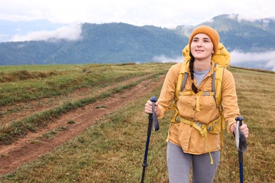 Young hiker with trekking poles and backpack in mountains outdoors, space for text