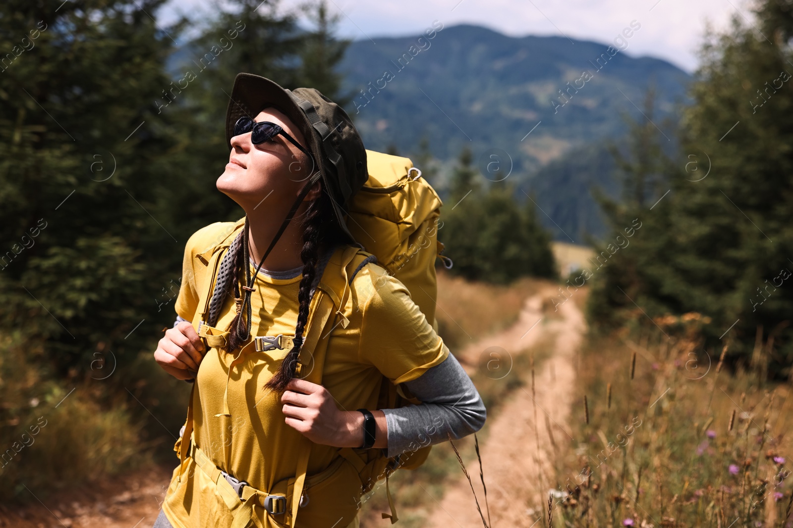 Photo of Young hiker with hat, sunglasses and backpack outdoors, space for text