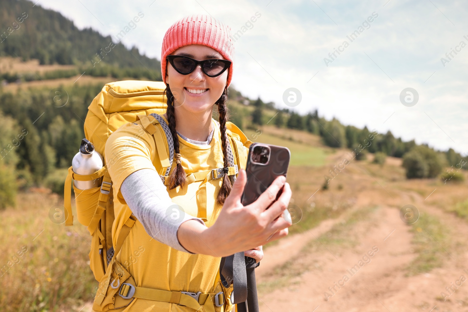 Photo of Young hiker with backpack taking selfie outdoors, space for text