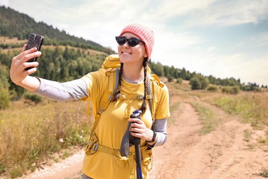 Young hiker with backpack taking selfie outdoors, space for text