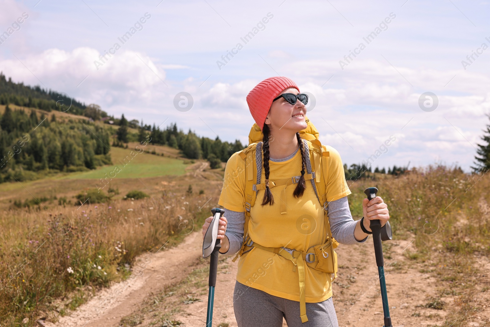 Photo of Young hiker with sunglasses, trekking poles and backpack outdoors, space for text