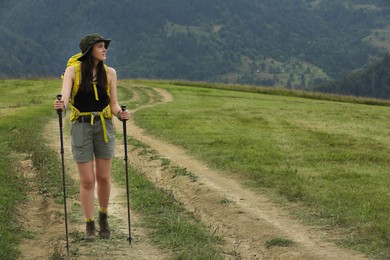 Young hiker with backpack and trekking poles in mountains, space for text