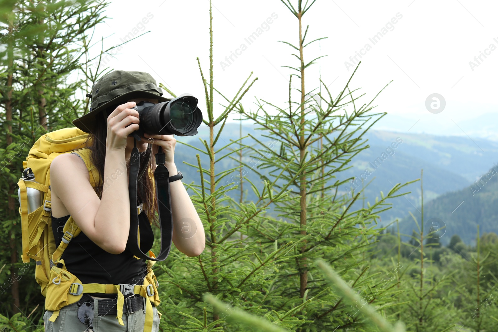 Photo of Young hiker with backpack and camera in forest, space for text