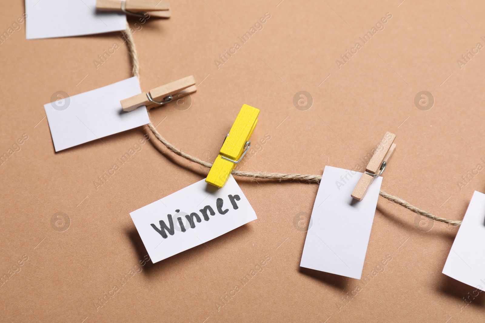 Photo of Paper note with word Winner among blank ones on rope against beige background, closeup