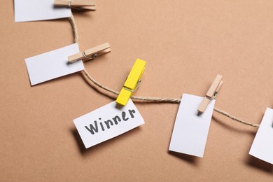 Photo of Paper note with word Winner among blank ones on rope against beige background, closeup