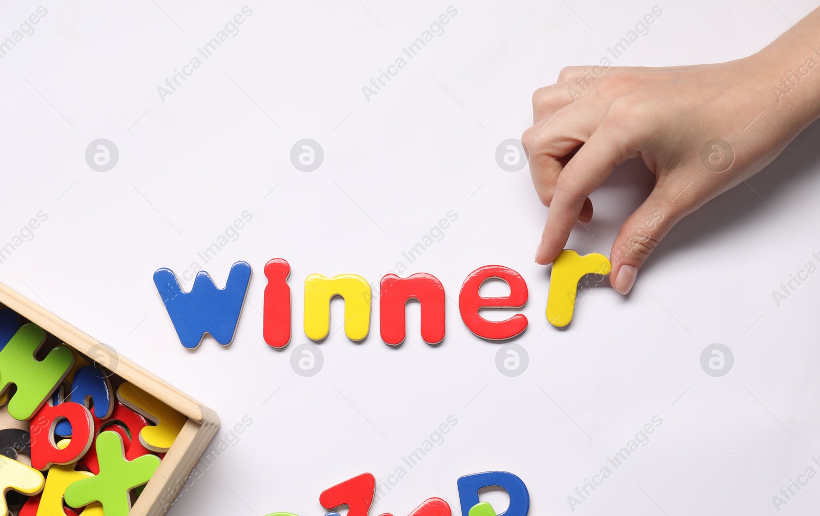 Photo of Woman making word Winner with magnetic letters on white background, top view