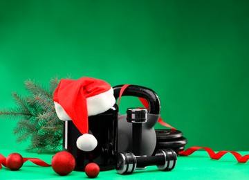 Photo of Dumbbells, kettlebell, container with supplement and Christmas decor on green background. Space for text