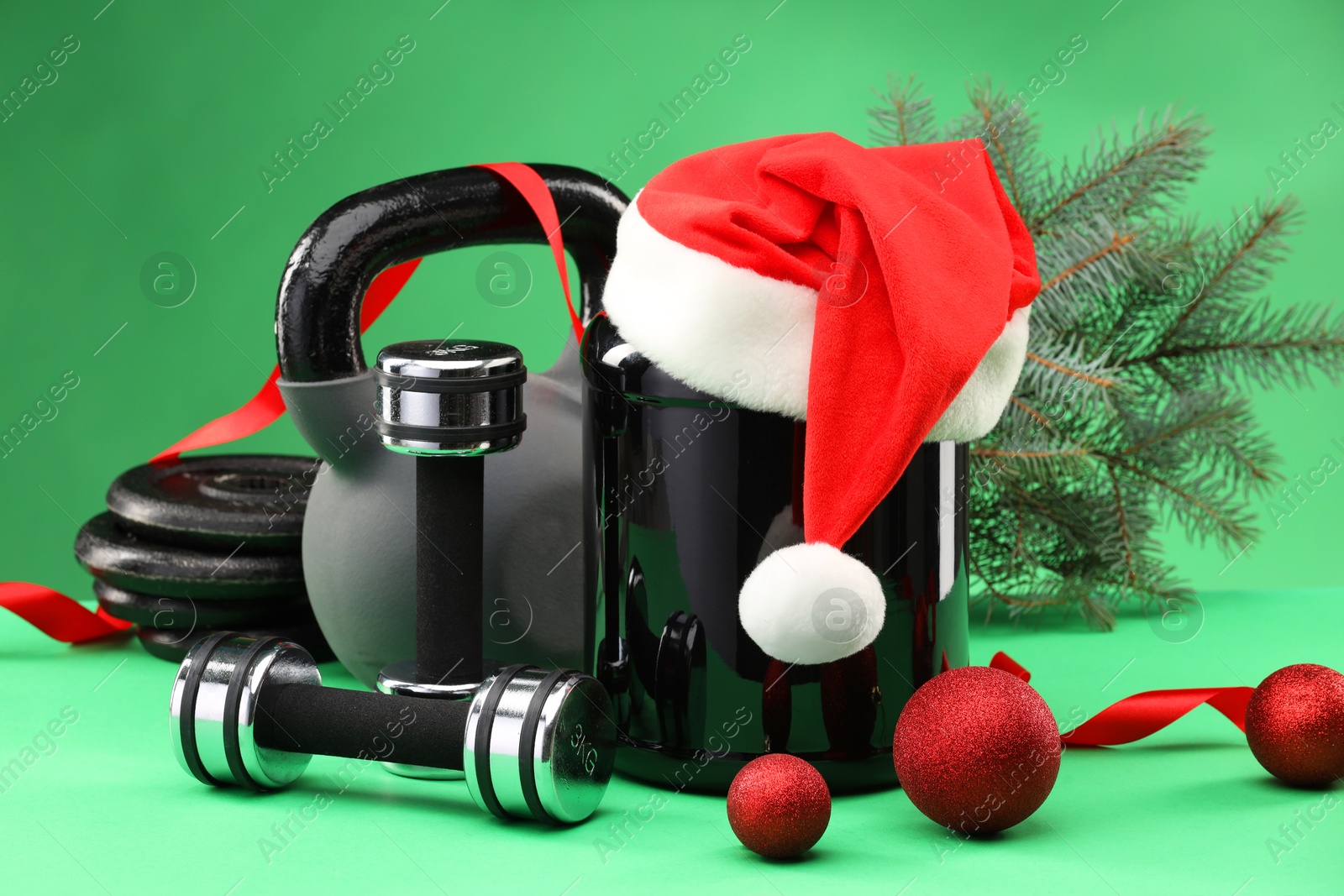 Photo of Dumbbells, kettlebell, container with supplement and Christmas decor on green background