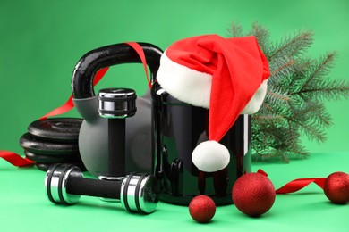 Photo of Dumbbells, kettlebell, container with supplement and Christmas decor on green background