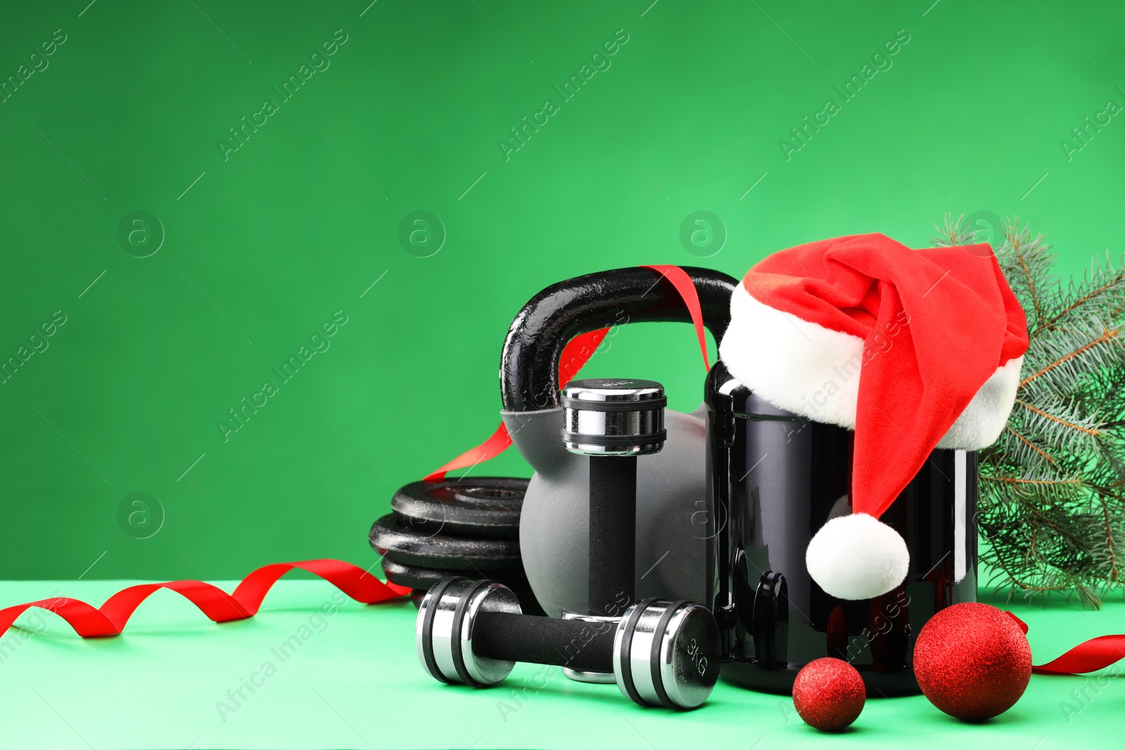 Photo of Dumbbells, kettlebell, container with supplement and Christmas decor on green background. Space for text