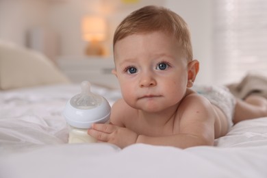 Photo of Cute little baby with bottle of milk on bed indoors