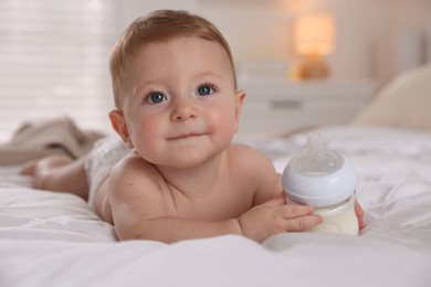 Cute little baby with bottle of milk on bed indoors