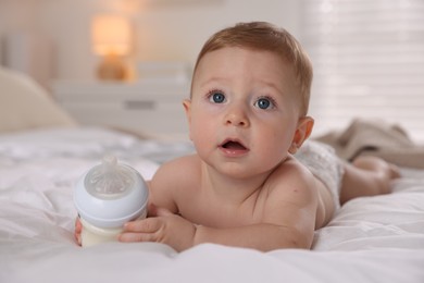 Photo of Cute little baby with bottle of milk on bed indoors