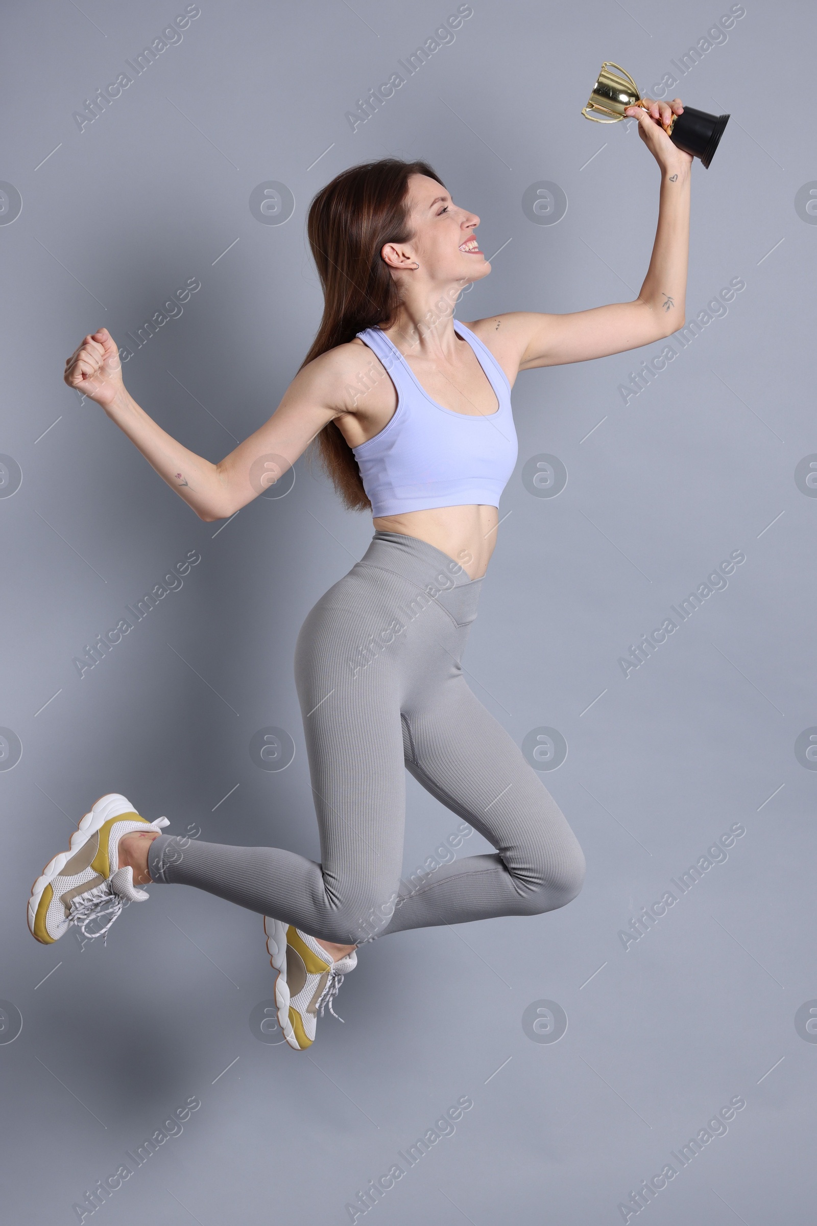 Photo of Happy winner with gold trophy cup jumping on gray background