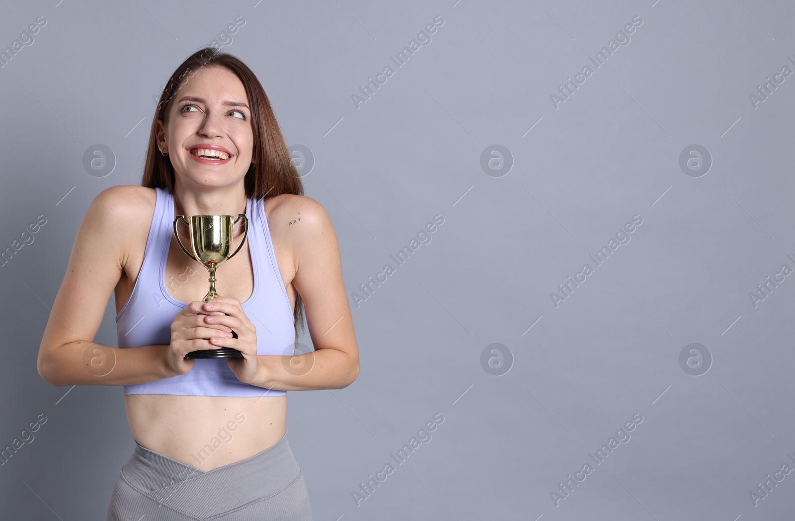 Photo of Happy winner with gold trophy cup on gray background, space for text