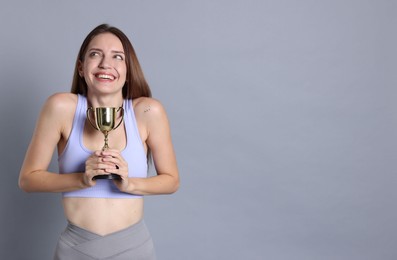 Happy winner with gold trophy cup on gray background, space for text