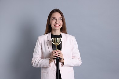 Photo of Happy winner with gold trophy cup on gray background