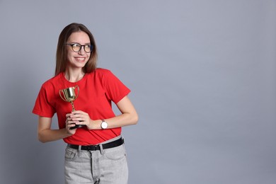 Photo of Happy winner with gold trophy cup on gray background, space for text