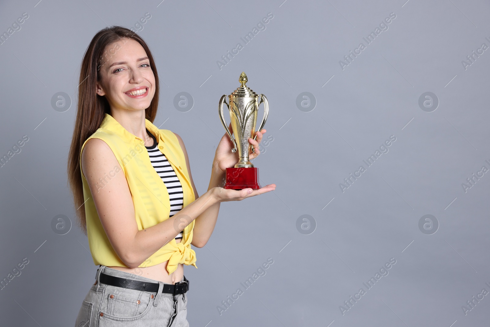 Photo of Happy winner with gold trophy cup on gray background, space for text