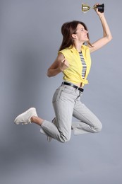 Photo of Happy winner with gold trophy cup jumping on gray background