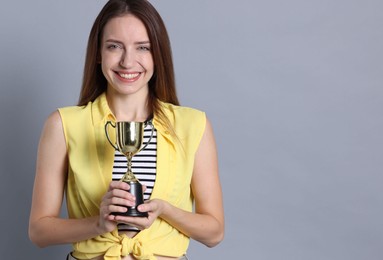 Photo of Happy winner with gold trophy cup on gray background, space for text