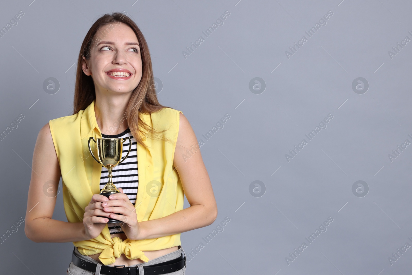 Photo of Happy winner with gold trophy cup on gray background, space for text