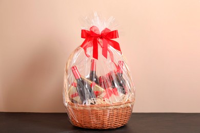 Wicker gift basket with wine on black textured table against beige background