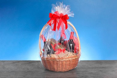 Photo of Wicker gift basket with wine on grey textured table against light blue background