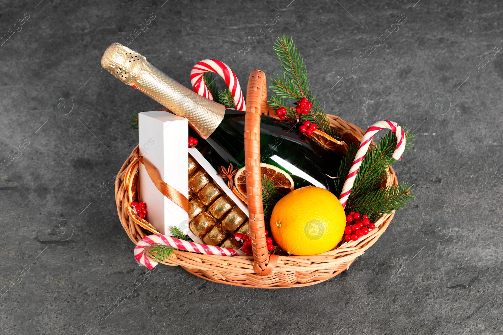 Photo of Wicker gift basket with sparkling wine and Christmas decor on grey textured table, above view