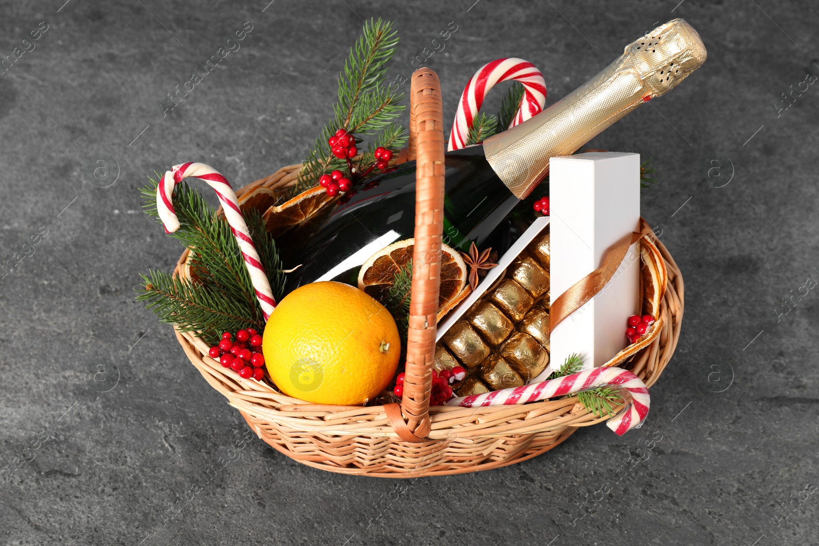 Photo of Wicker gift basket with sparkling wine and Christmas decor on grey textured table