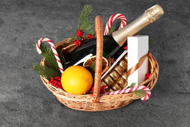 Photo of Wicker gift basket with sparkling wine and Christmas decor on grey textured table