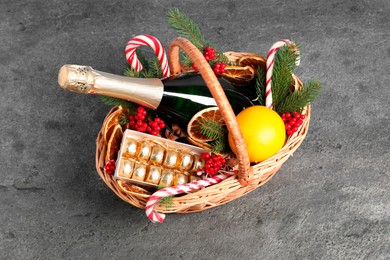 Photo of Wicker gift basket with sparkling wine and Christmas decor on grey textured table, above view