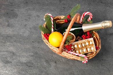 Photo of Wicker gift basket with sparkling wine and Christmas decor on grey textured table, above view. Space for text