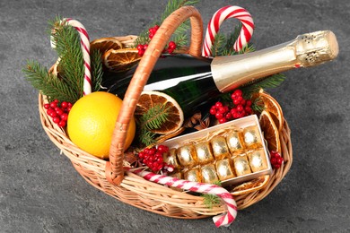 Wicker gift basket with sparkling wine and Christmas decor on grey textured table