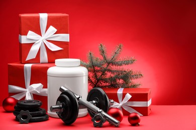 Photo of Dumbbells, container with supplement and Christmas decor on red background. Space for text