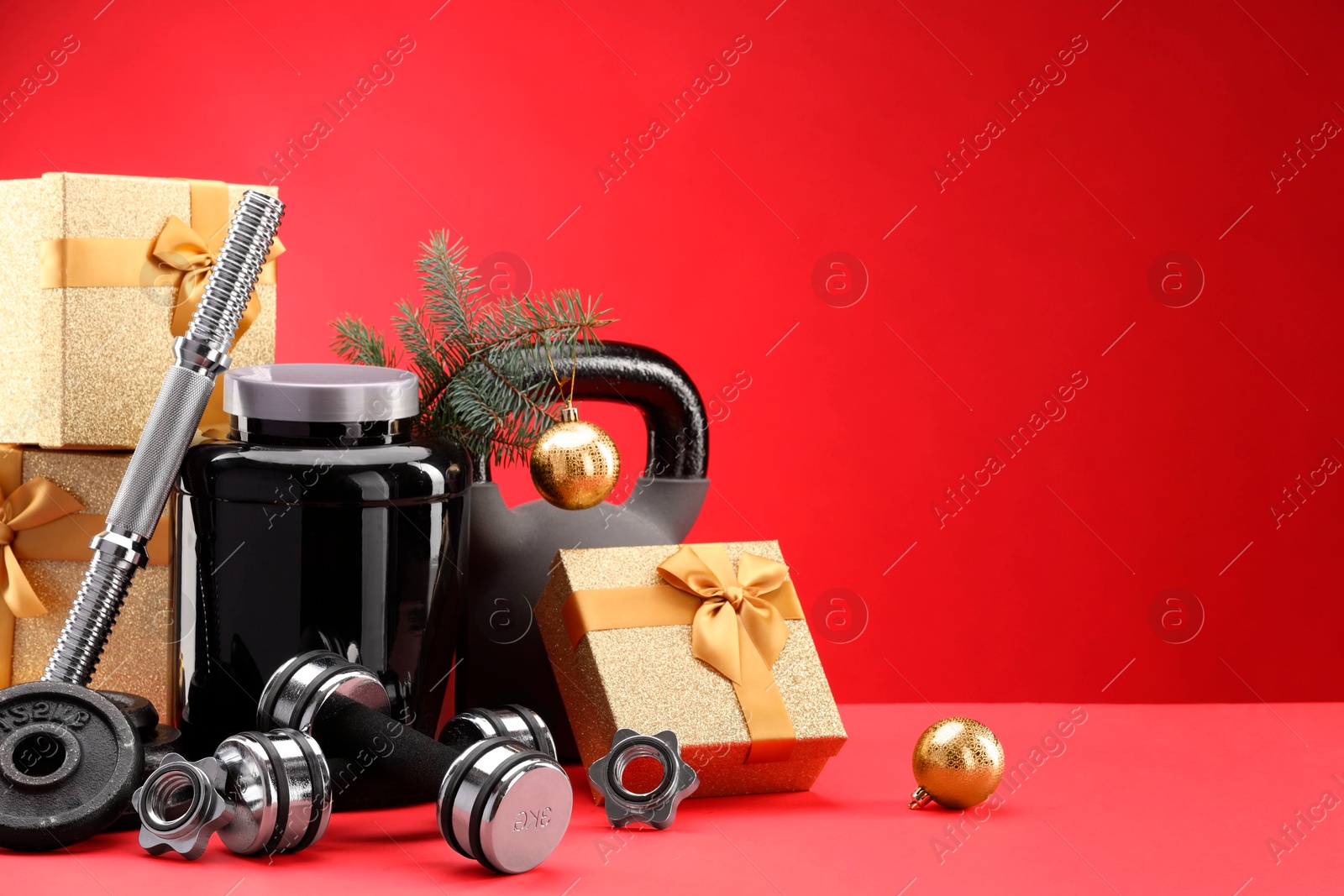 Photo of Dumbbells, kettlebell, container with supplement and Christmas decor on red background. Space for text