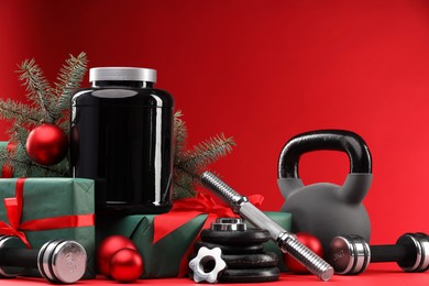 Photo of Dumbbells, kettlebell, container with supplement and Christmas decor on red background