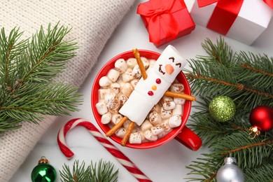 Photo of Funny snowman made with marshmallows in cup of hot drink and Christmas decor on white table, flat lay