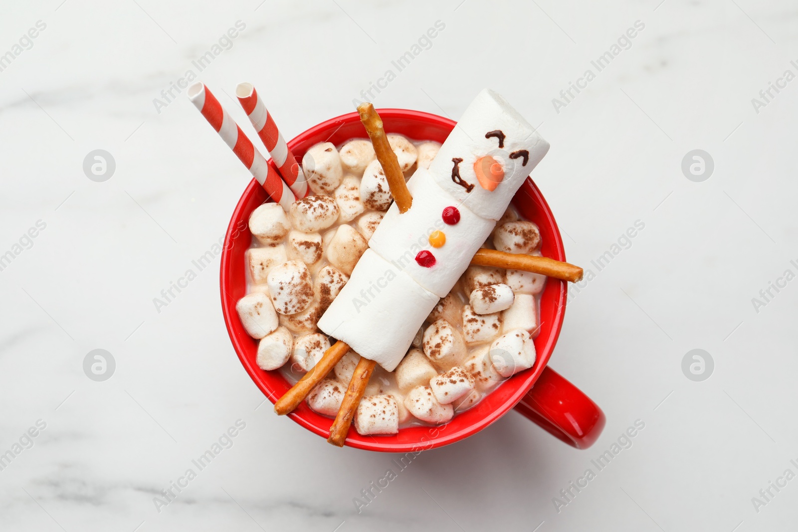 Photo of Funny snowman made with marshmallows in cup of hot drink on white table, top view