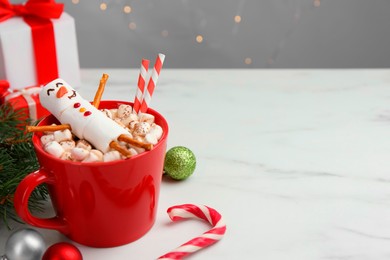 Photo of Funny snowman made with marshmallows in cup of hot drink and Christmas decor on white table. Space for text