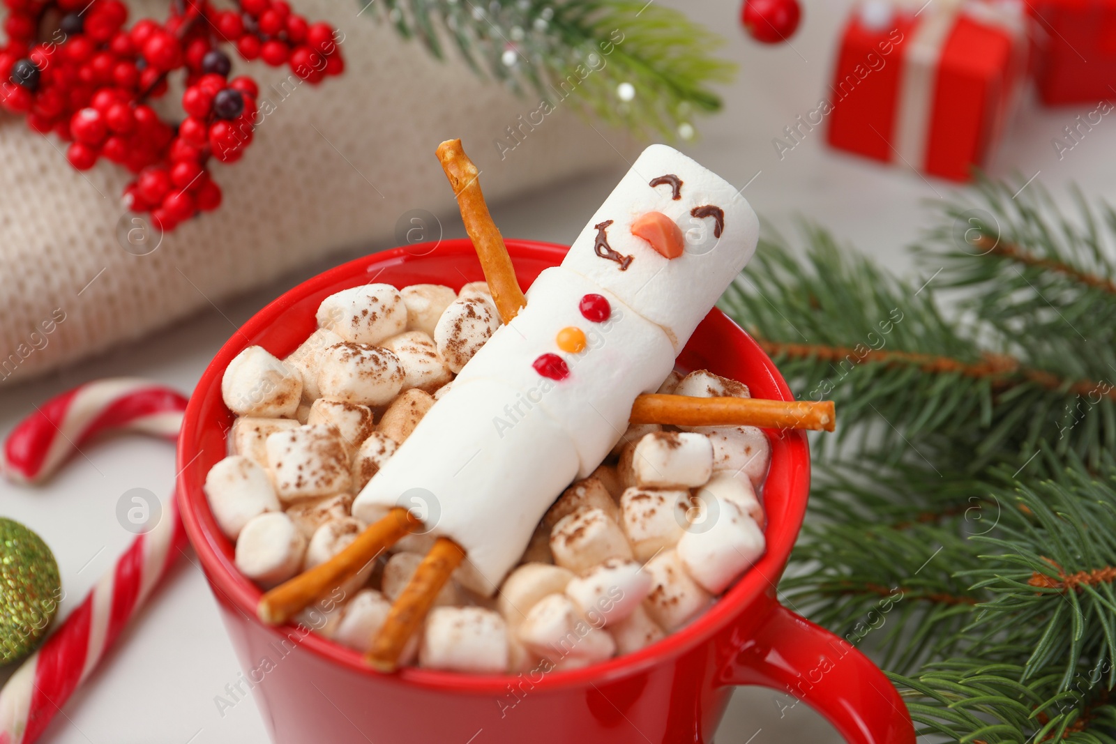 Photo of Funny snowman made with marshmallows in cup of hot drink and Christmas decor on white table, closeup