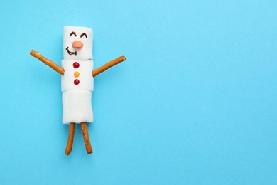 Photo of Funny snowman made of marshmallows on light blue background, top view. Space for text