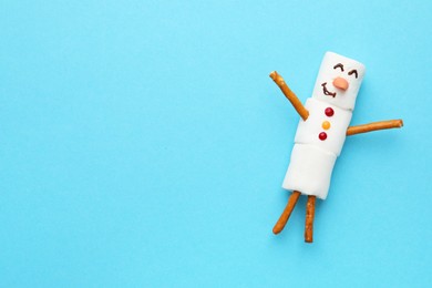 Photo of Funny snowman made of marshmallows on light blue background, top view. Space for text