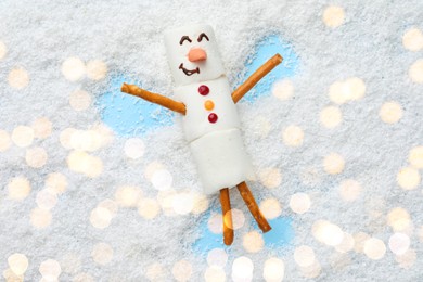 Photo of Marshmallow snowman making angel on artificial snow, top view