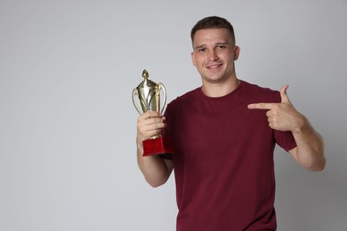 Happy winner with golden trophy cup on light grey background, space for text