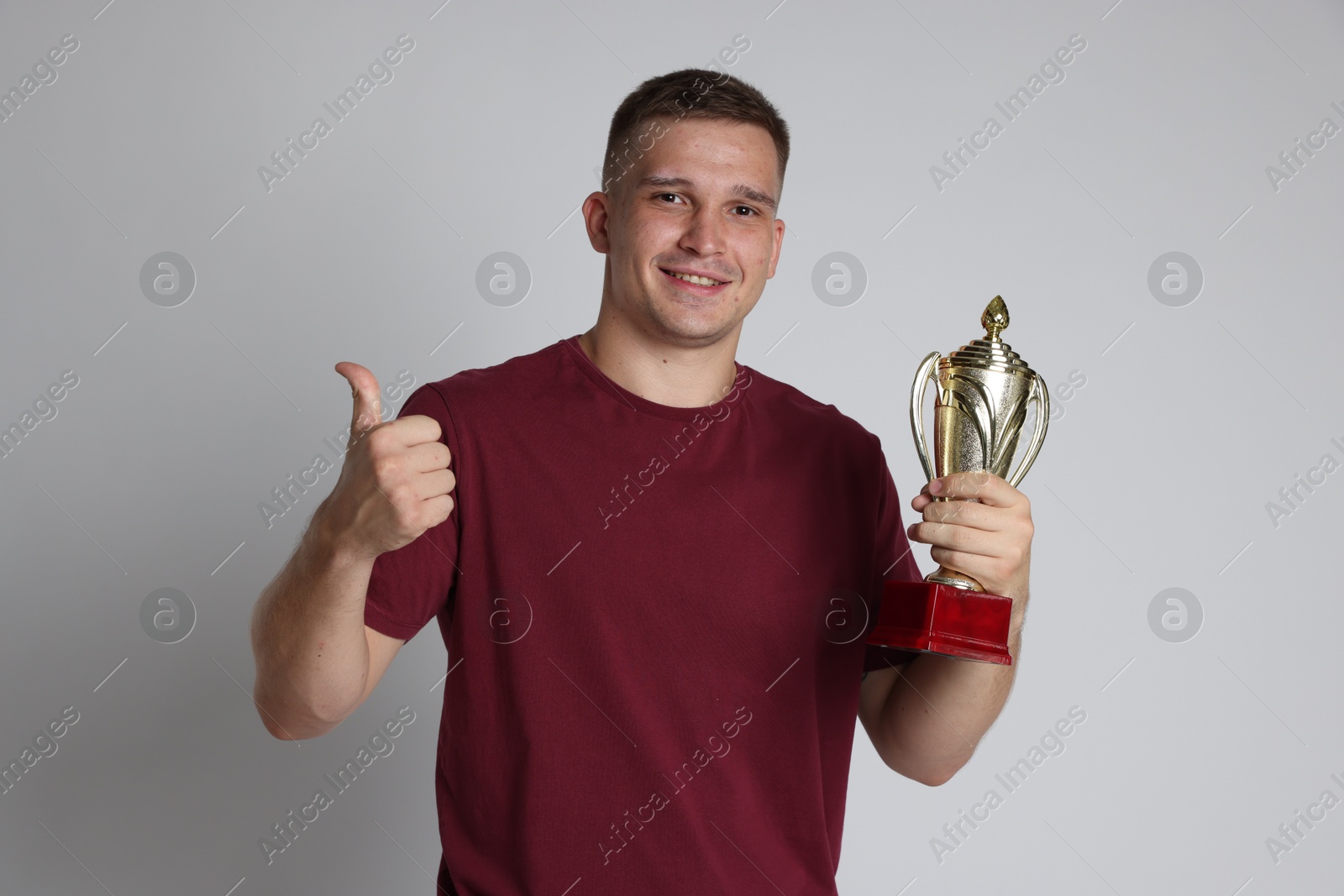 Photo of Happy winner with golden trophy cup showing thumbs up on light grey background